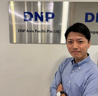 会社エントランスの前で腕を組むTさんの写真