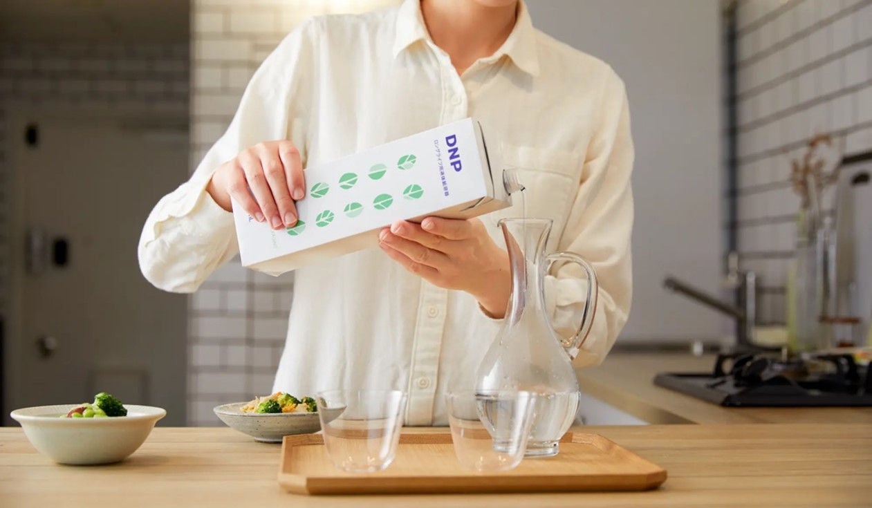 Person pouring a beverage from the liquid packaging carton for long shelf life into glassware on a kitchen counter