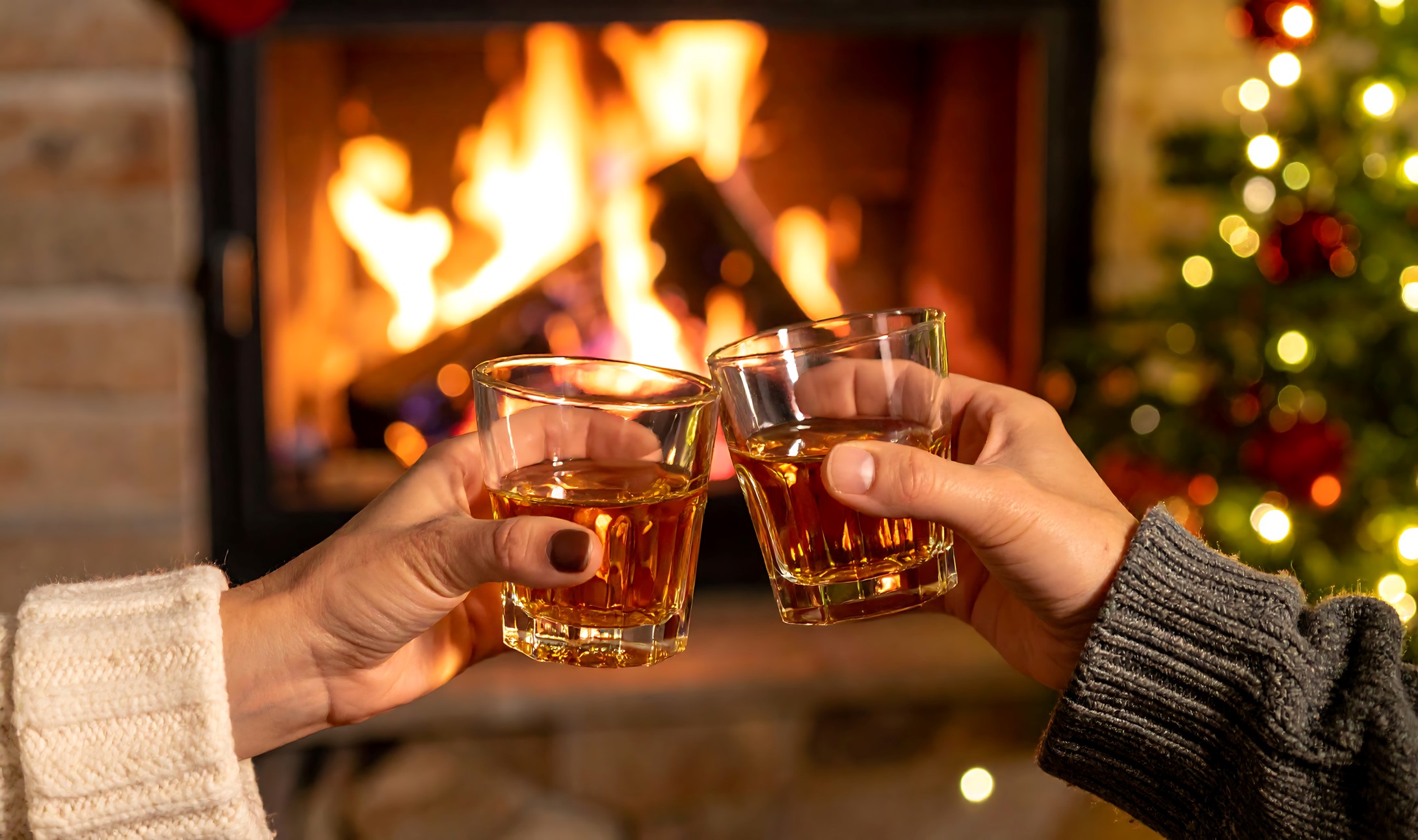 Two people toasting glasses of high-proof spirits by a fireplace, representing use of the liquid packaging carton for alcoholic beverages